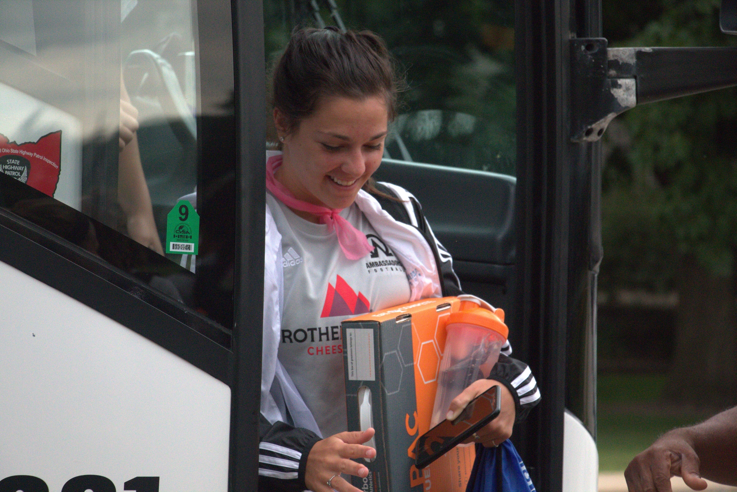 Woman holding a large orange box with 'Rother' branding, standing next to a vehicle.