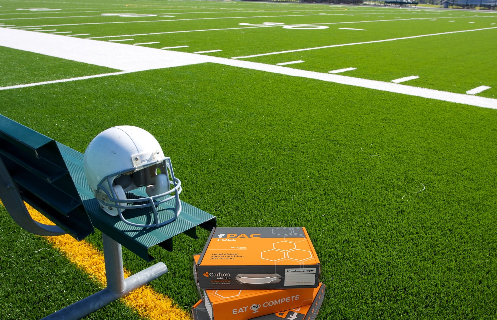 Helmet on a football stand with a box labeled 'Eat to Compete' on a football field.