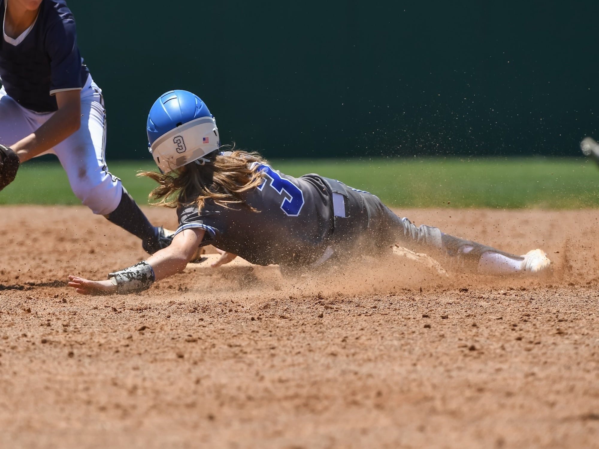 Baseball player sliding into a base with another player attempting to tag them out on a baseball field.