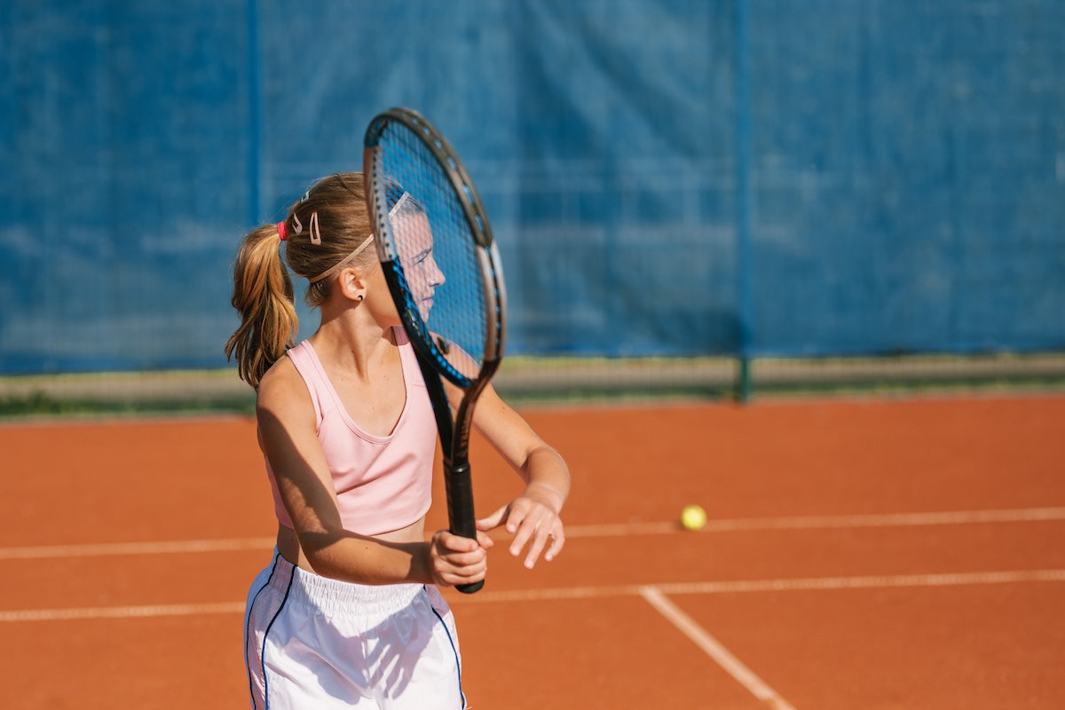 Woman holding a tennis racket on a clay court with a blue tarp in the background