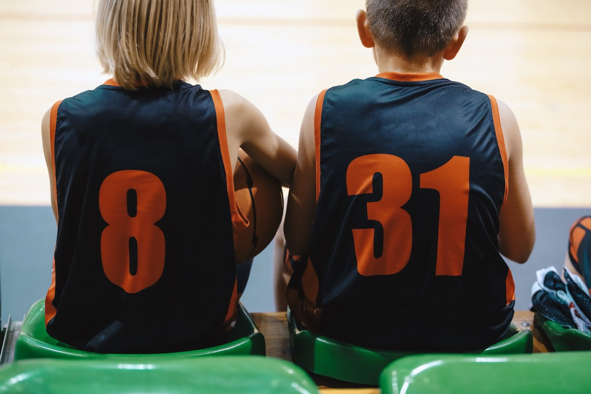 Two people wearing basketball jerseys with numbers 8 and 31 sitting on green chairs.