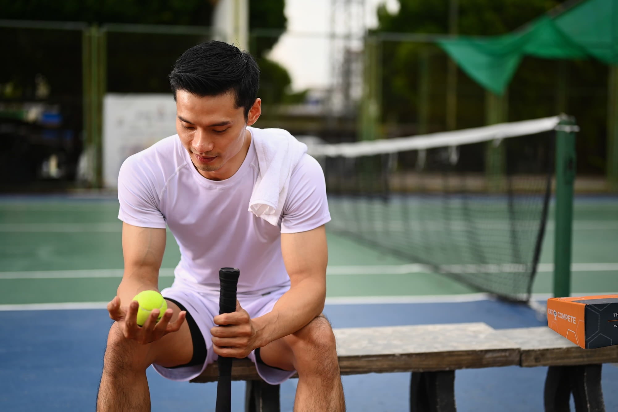 Man sitting on a bench with a tennis ball and racket on a tennis court