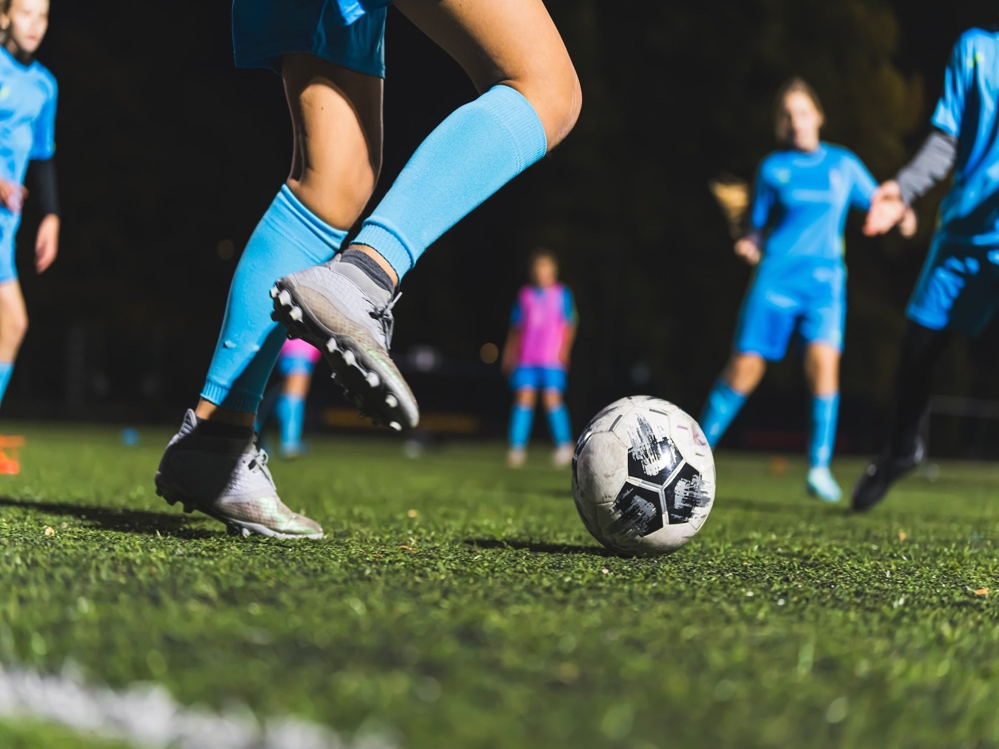 Soccer player in action with ball on a grass field, other players in the background