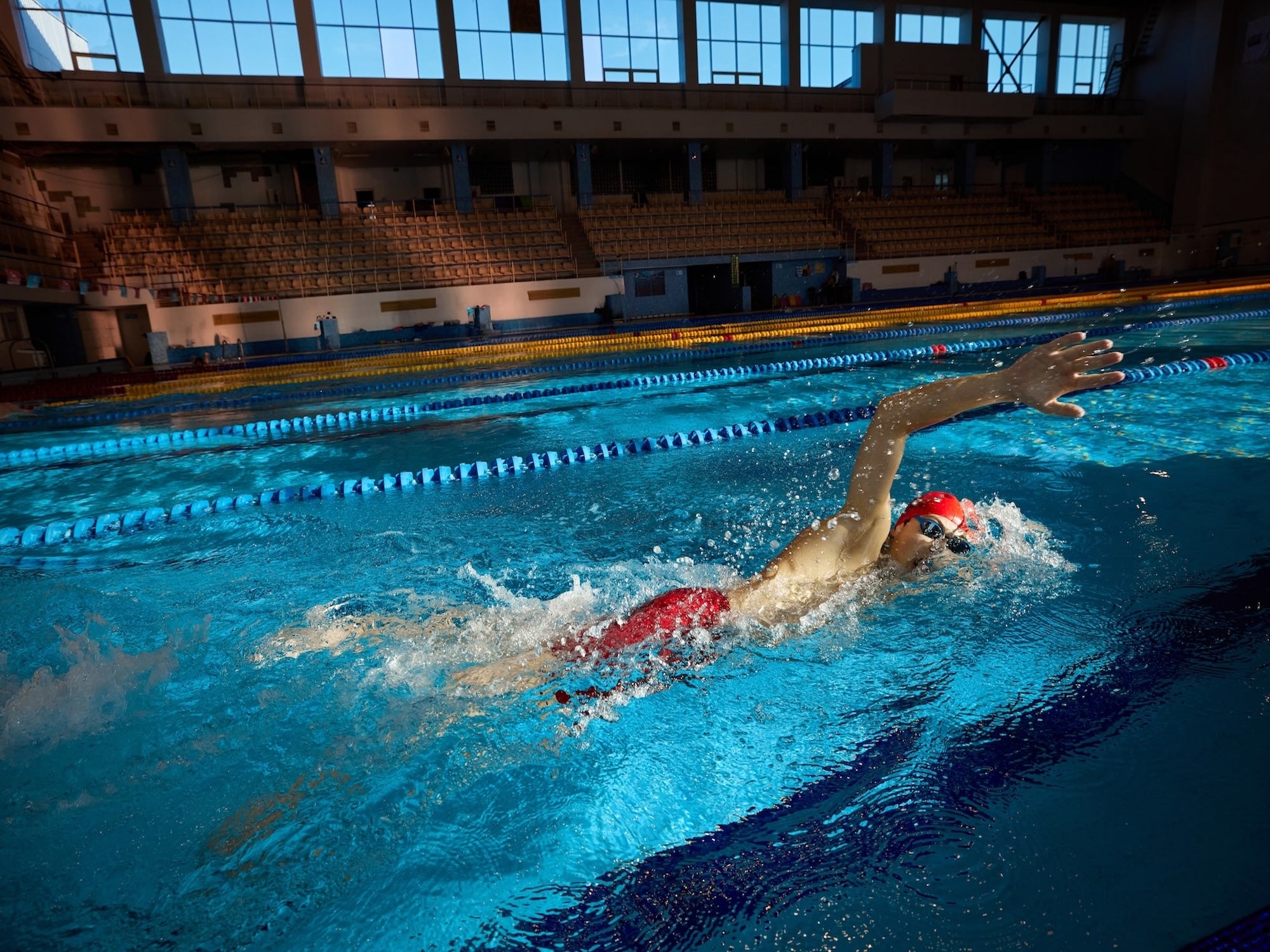 Person swimming in a pool with lanes and spectator stands in the background
