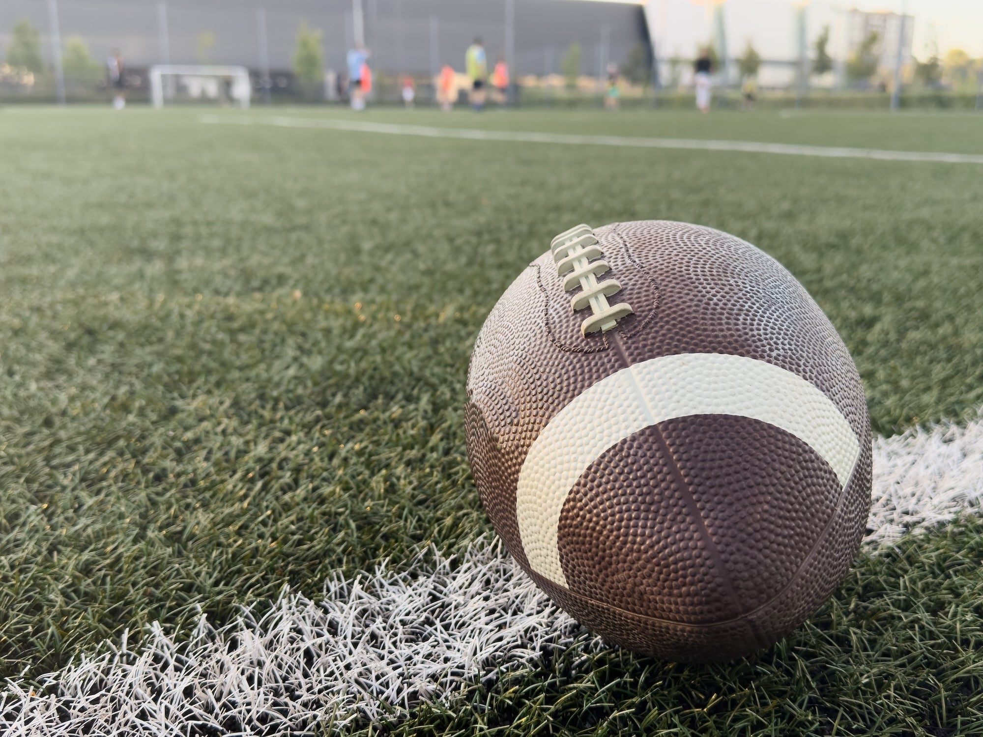 Football on a grass field with a blurred sports facility in the background
