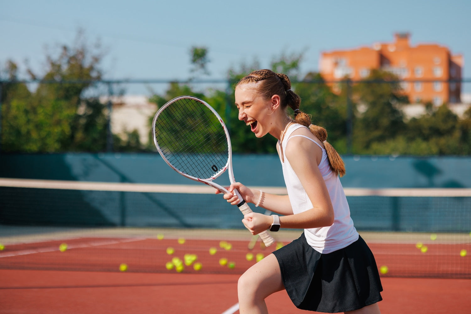 Woman playing tennis on a court with trees and buildings in the background
