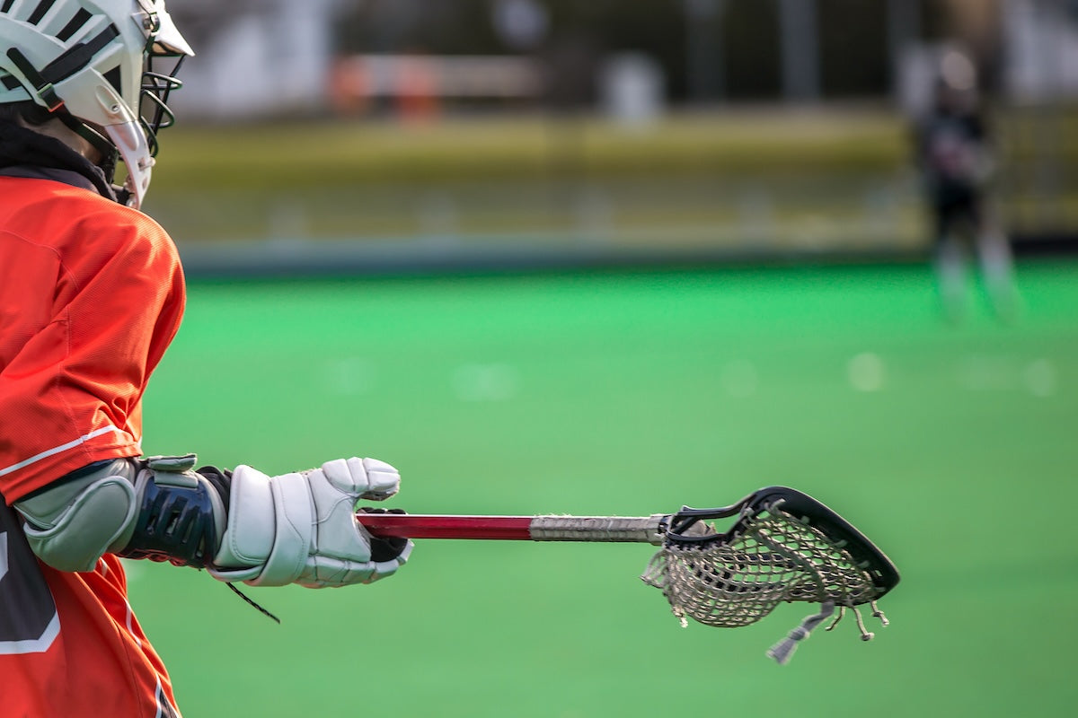 Person holding a lacrosse stick on a green field