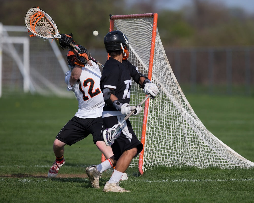 Two lacrosse players in action near a goal on a field